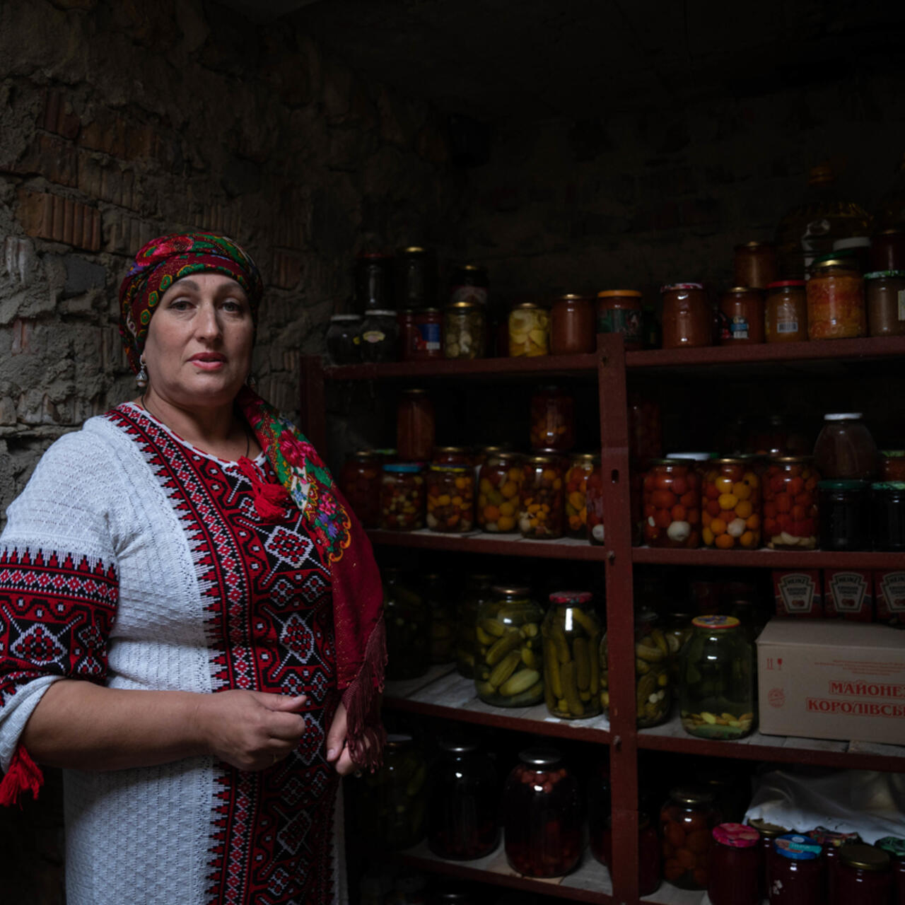 Woman standing in a storage room with preserved food in jars behind her